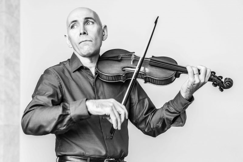 Enrico Onofri medio cuerpor tocando violín blanco y negro